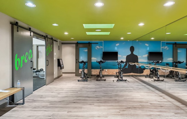 A gym with exercise bikes and a green logo on the wall.