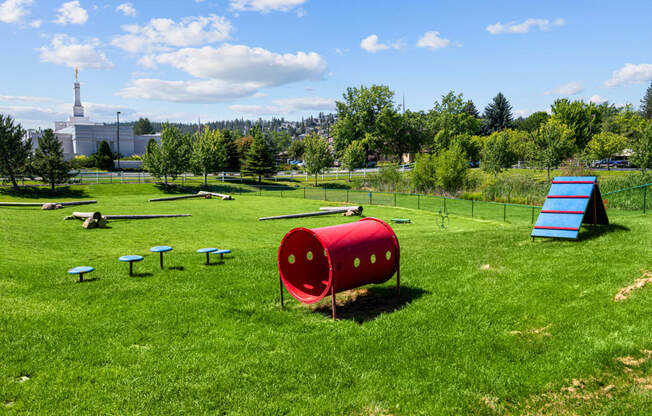 a playground with a seesaw and a red barrel in a field