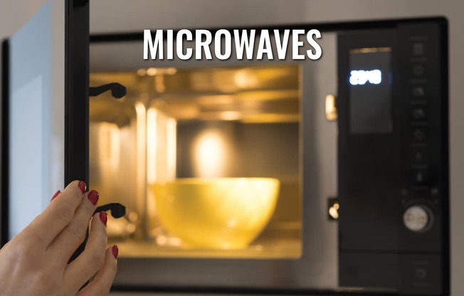A person is holding a spoon in front of a microwave with a bowl inside.