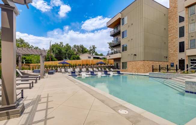 a swimming pool with lounge chairs and umbrellas next to a building