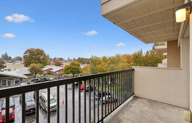 A balcony with a black railing overlooks a parking lot and trees.