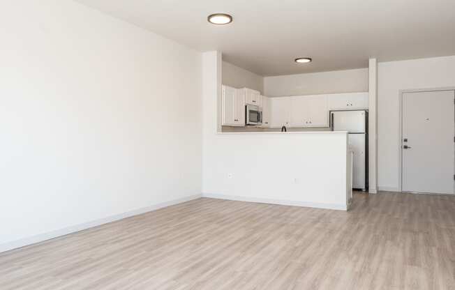 an empty living room and kitchen with white walls and wood flooring