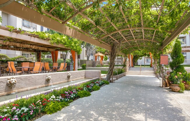a courtyard with a pergola and flowers and benches at La Ventura Apartments, Plano, 75093