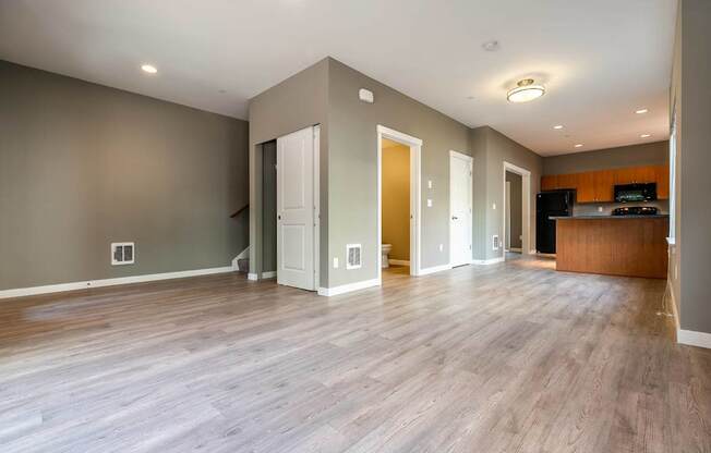 A spacious room with wooden floors and a kitchen area in the background.