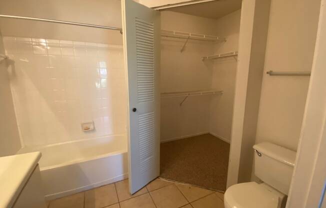 Bathroom with tile floors, toilet, shower tub combo with tile back splash, towel bar, white cabinets and view of closet