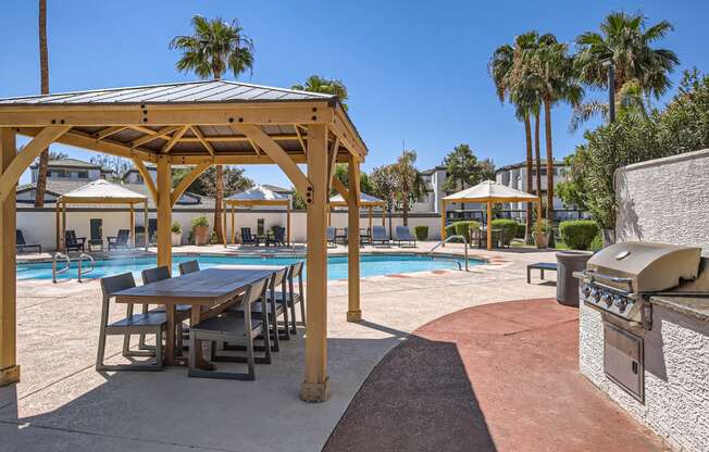 a picnic table and grill next to a pool with palm trees in the background