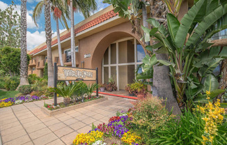 a building with a sign in front of a flower garden at Villa La Paz Apartments, Bellflower