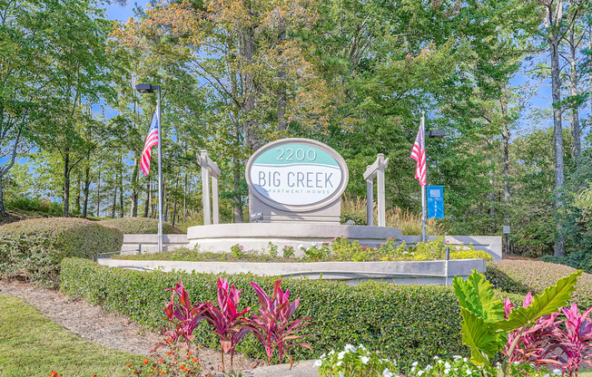 A sign for Big Creek stands in a garden with flowers and trees in the background.