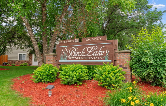 A sign for Will Branch Lake Townhomes Rentals is surrounded by greenery and flowers.