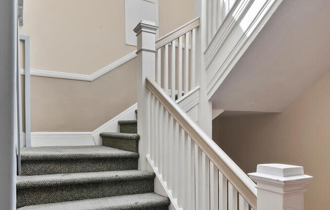A staircase with a grey carpeted runner and white balusters at Brookmore Apartments