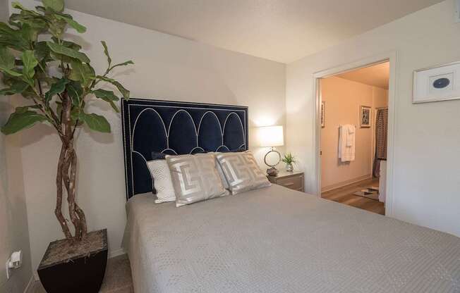 A bedroom with a bed, pillows, a plant, and a mirror at Autumn Oaks Apartments, Roseville, CA, 95678