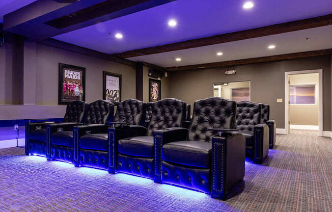 A row of black leather chairs are lined up in a room with purple lighting.