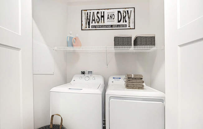 A laundry area with a washer and dryer and a shelf above them at Andover Pointe Apartment Homes, La Vista, NE, 68138