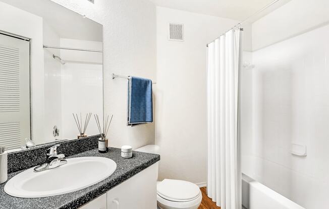 Virtually staged bathroom with white shower curtain over tiled tub, gray countertop, white cabinetry and large mirror