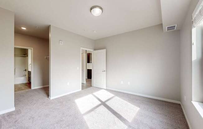 A spacious room with a carpeted floor and a window on the right side.