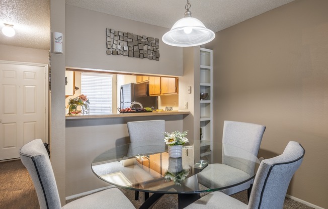 A dining room with a glass table and grey chairs.