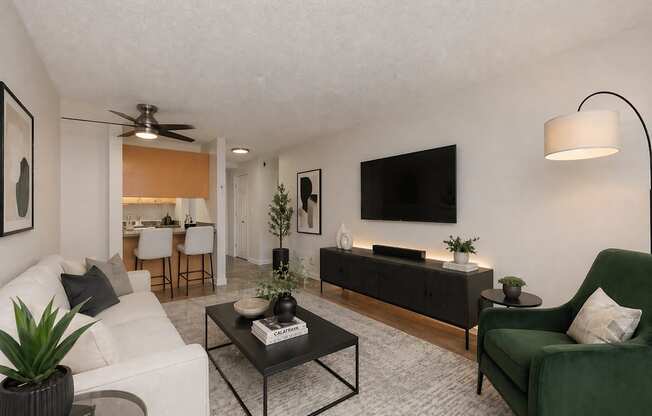 A living room with a white couch, a green armchair, a black coffee table, and a flat-screen TV mounted on the wall.