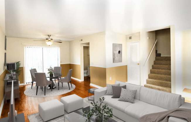 A living room with a white couch, a dining table with chairs, a rug, and a ceiling fan.