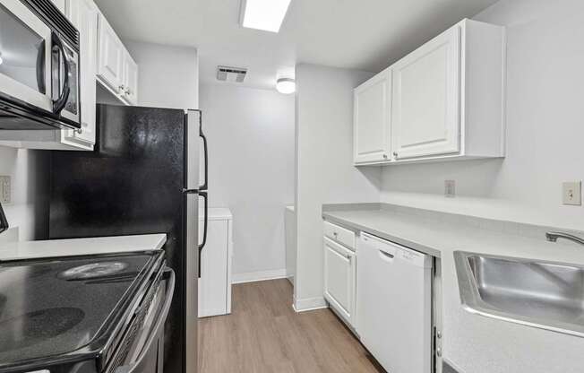A black refrigerator sits in a kitchen with white cabinets and a stove top oven.