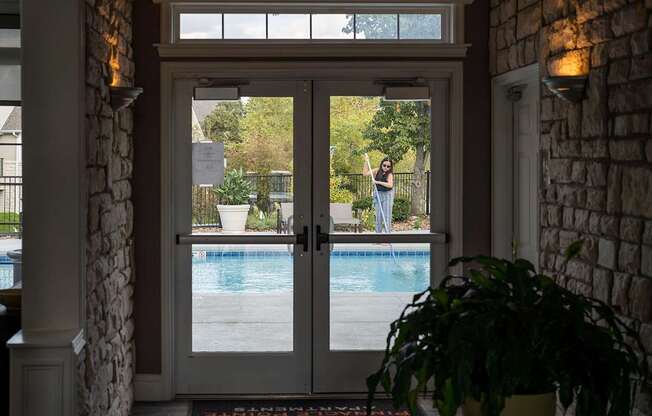 A woman is standing in the doorway of a house with a pool in the backyard.