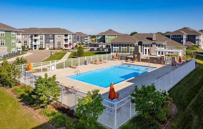 A large swimming pool surrounded by a white fence and a grassy area with trees.