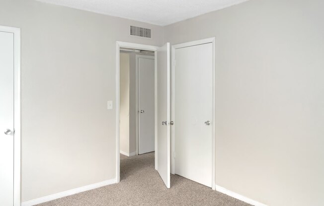 A bedroom with a carpeted floor and three doors.