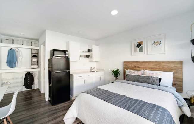 A bedroom with a bed, a chair, and a fridge.