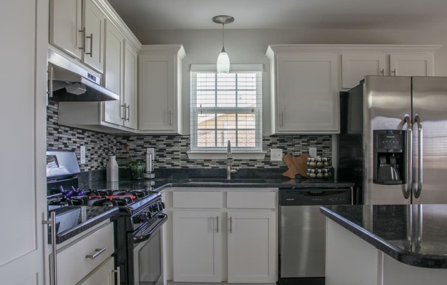 a kitchen with white cabinets and black countertops and splash guards at Village of Cottonwood Springs
