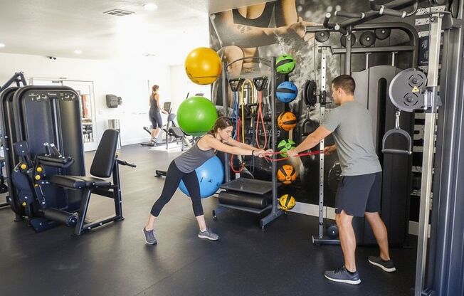 A man and woman are working out in a gym with various exercise equipment.