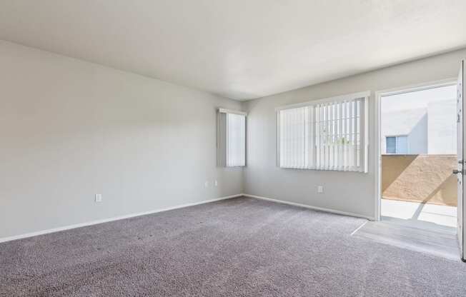 the living room of an apartment with carpet and a door to the patio