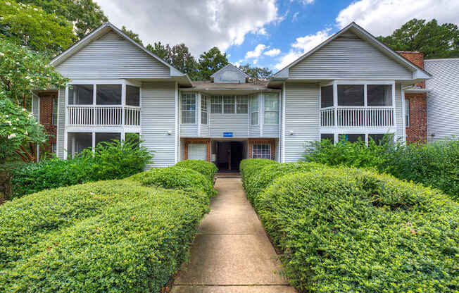 A two-story house with a driveway and hedges.