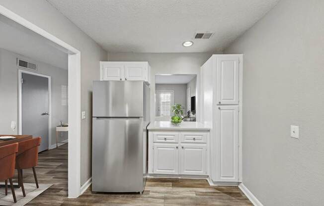 A kitchen with a refrigerator, cabinets, and a dining table.