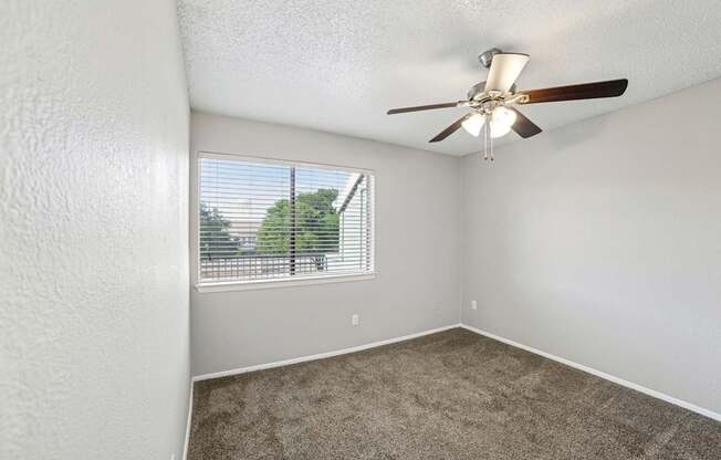 A room with a ceiling fan and a window with blinds.