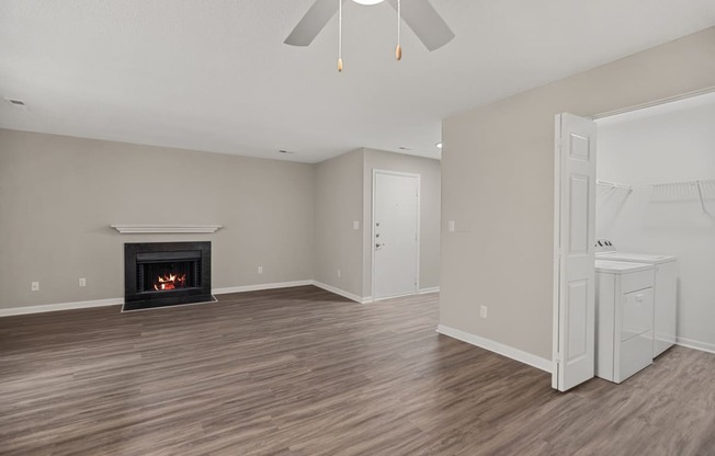 an empty living room with a fireplace and a white kitchen