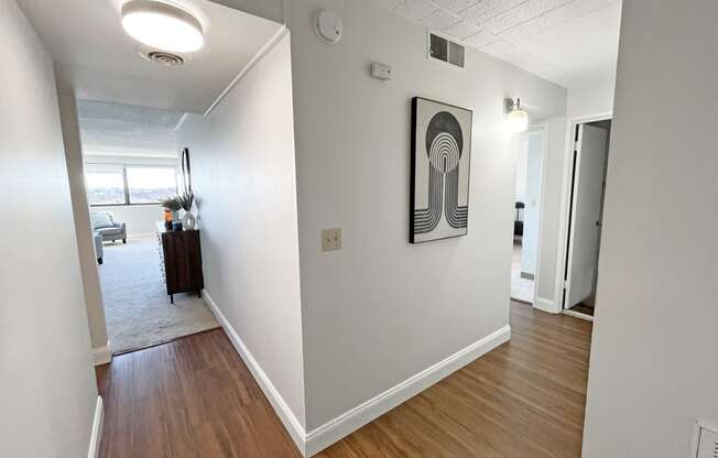 a view of the hallway of an apartment with hardwood floors and a painting on the wall
