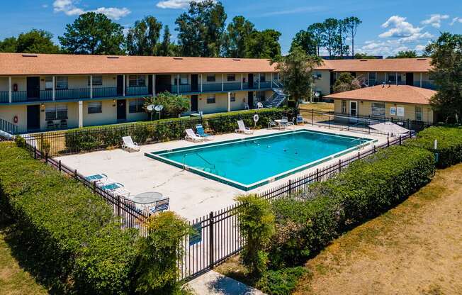 A swimming pool surrounded by a fence and bushes in front of a building.