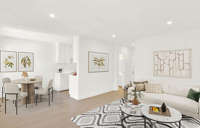 A living room with a white couch, a dining table with chairs, and a rug on the floor.