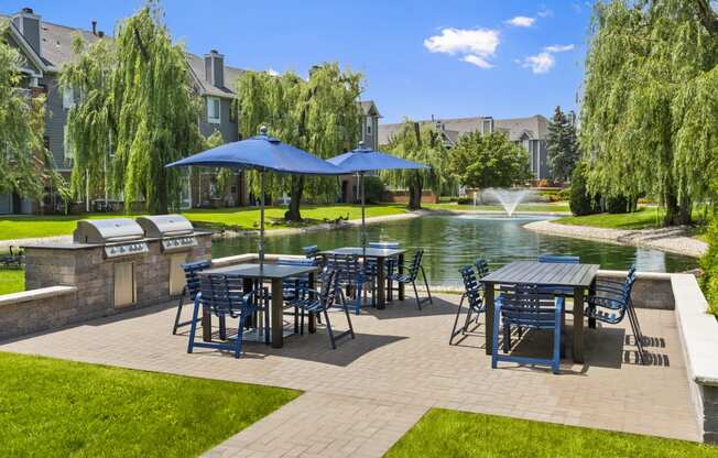 a patio with tables and chairs and umbrellas next to a pond
