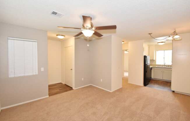 an open living room with a ceiling fan and a kitchen in the background