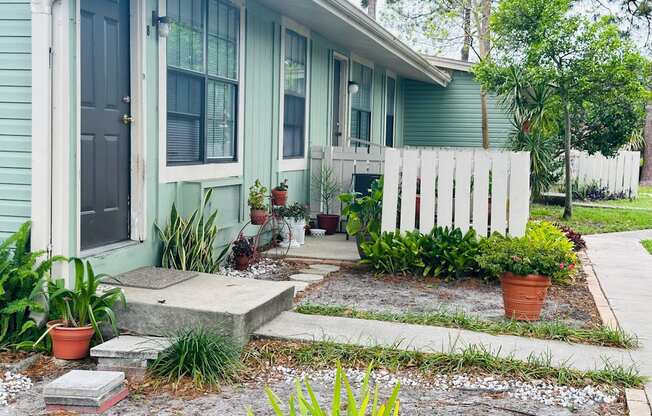 a blue house with a white fence and plants in front of it