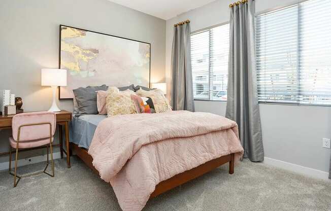 A bedroom with a bed, desk, chair, and a large painting on the wall.