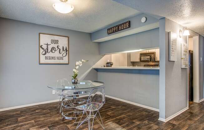 a dining area with a glass table and chairs and a kitchen in the background