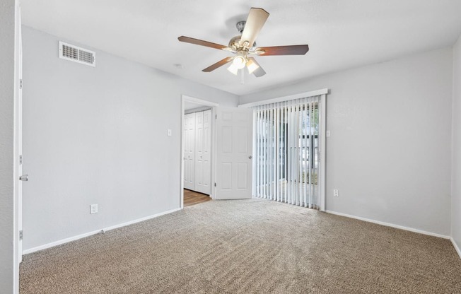 an empty living room with a ceiling fan and a door to a balcony