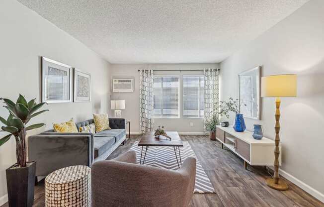 A living room with a grey couch, a brown chair, a wooden floor, and a large window.