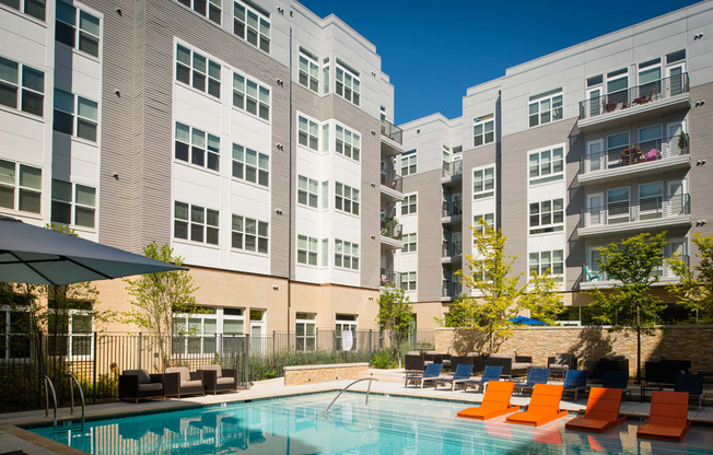 a swimming pool with orange chairs in front of an apartment building