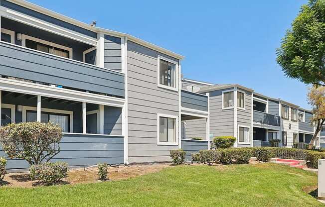 A row of grey and blue houses with green lawns in front.