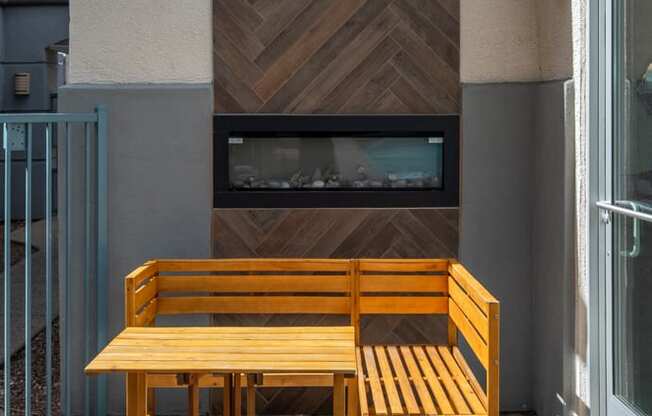 a wooden table and bench sit on a balcony in front of a fireplace