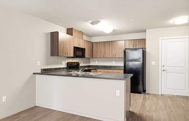A kitchen with a black fridge and wooden cabinets.