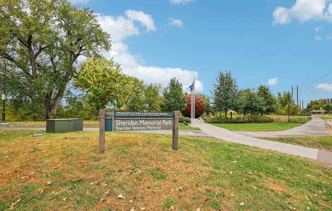 A sign for Sheridan Memorial Park is in front of a green box and a tree.