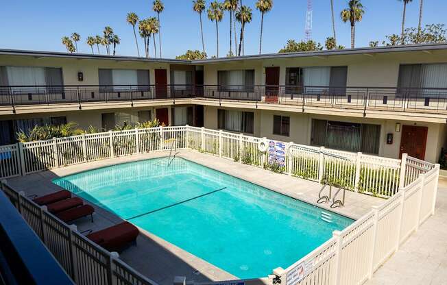 A pool surrounded by a white fence and red lounge chairs.